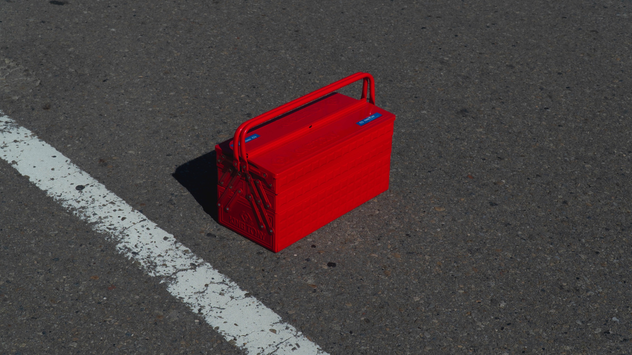 Red King Tony cantilever toolbox photographed on asphalt beside a white road marking