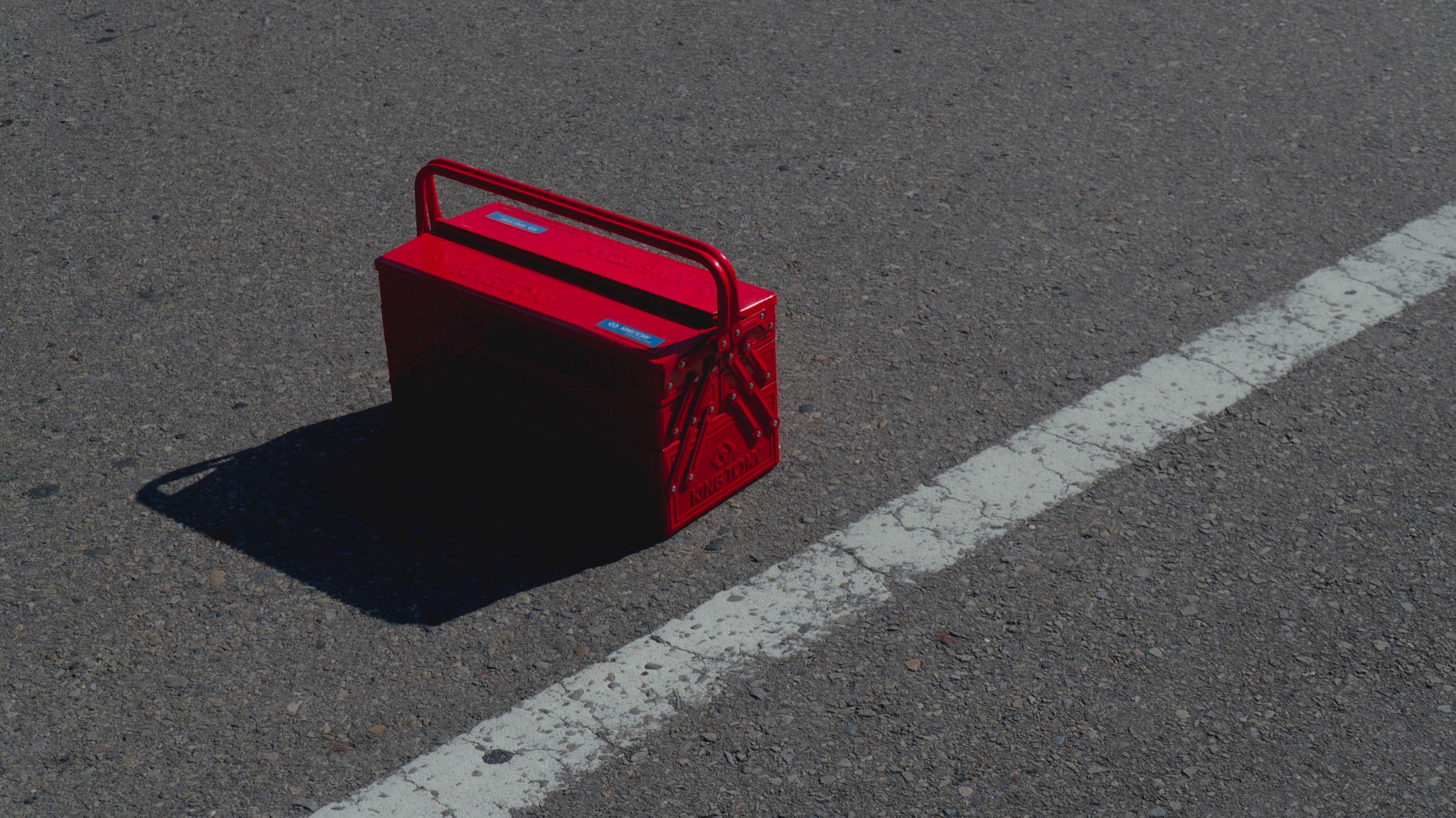 Red King Tony cantilever toolbox casting a long shadow on asphalt